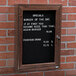 A black Aarco enclosed message board with white text on it.