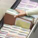 A hand picking up a file folder from a file drawer with several file folders inside.