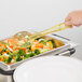 A person uses a Cambro amber perforated spoon at a salad bar to serve vegetables.