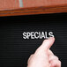 A person's thumb pointing to a black letter board with cherry frame.
