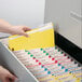 A hand putting a yellow Smead fastener folder into a file cabinet.