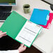 A person holding a green Smead file folder with papers inside.