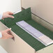 A person's hand opening a green Smead file folder in a file drawer.