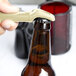 A hand using a Franmara beige plastic bottle opener to open a brown beer bottle.