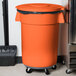 A Carlisle orange trash can lid on a black trash can.
