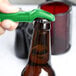A hand using a green Franmara Traveler's Lime plastic bottle opener to open a brown bottle.