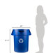 A woman standing next to a blue Rubbermaid Brute recycling can.
