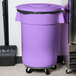 A Carlisle purple trash can lid on a black trash can.
