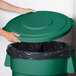 A hand placing a green lid on a green trash can.
