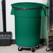 A green Carlisle Bronco trash can lid on a black trash can.