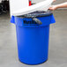 A hand putting a white plastic lid on a blue Continental Huskee trash can.