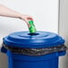 A hand throws a green can into a blue Rubbermaid recycling lid.