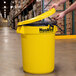 A man opening a yellow Continental Huskee trash can in a warehouse.