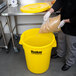 A person pouring food into a yellow Continental Huskee trash can.