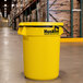 A yellow Continental Huskee round trash can with a yellow lid in a warehouse.