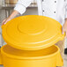 A person holding a Carlisle yellow flat round trash can lid.