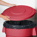 A person's hand holding a red Carlisle trash can lid.