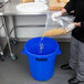 A person pouring pasta into a blue Continental Huskee recycling/trash can.