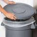 A person's hand opening a Carlisle grey trash can lid.