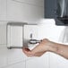 A hand using a Lavex stainless steel horizontal soap dispenser on a wall.