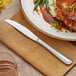 An Acopa Edgeworth stainless steel dinner knife on a plate with meat, green beans, and sauce.