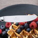 A Chef & Sommelier stainless steel dessert knife on a plate of waffles with berries.