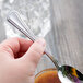 A hand holding a Libbey stainless steel teaspoon.