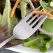 An Arcoroc stainless steel salad fork with a carrot stick on it next to a salad.