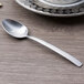 An Arcoroc stainless steel demitasse spoon with a silver handle on a table.