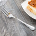 A Libbey stainless steel dessert fork next to a piece of cake on a table.