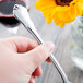 A hand holding a Libbey stainless steel dessert fork with a yellow flower in the background.