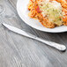 A Libbey stainless steel dinner knife with a fluted blade on a plate of spaghetti with cheese and meat.