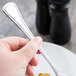 A person holding a Libbey stainless steel dinner fork over a plate of food.
