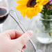 A person holding a Libbey Lady Astor stainless steel utility/dessert fork over a table with a flower.