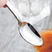 A hand holding a Libbey stainless steel dessert spoon over a glass of liquid.