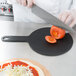 A person using an Epicurean slate pizza board to cut a tomato on a pizza.