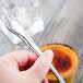 A hand holding a Libbey Lady Astor stainless steel dessert spoon over a glass of liquid.