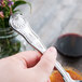 A hand holding a Libbey silver stainless steel teaspoon.