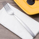 An Arcoroc stainless steel dinner fork on a napkin next to a plate of food.