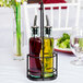 A Tablecraft black olive oil cruet rack holding oil and vinegar bottles on a table.