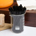 An American Metalcraft beaker glass filled with black straws on a counter.
