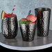 Three American Metalcraft hammered black Moscow Mule cups filled with ice and watermelon.