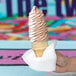 A hand holding a white Choice luncheon napkin folded into a cone with brown and white soft serve ice cream.