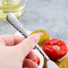 A person holding a Libbey stainless steel cocktail fork with tomatoes and olives.