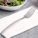 An Arcoroc stainless steel salad fork on a napkin next to a bowl of salad.
