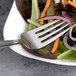 A Arcoroc stainless steel salad fork in a bowl of salad with a carrot stick.