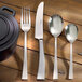 A set of Arcoroc Latham Sand stainless steel dessert spoons on a wood surface.