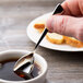 A person holding a Chef & Sommelier stainless steel demitasse spoon in a cup of coffee.