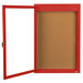 A red enclosed bulletin board with a white cork board behind a glass door.