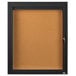 A black framed Aarco indoor bulletin board cabinet with a glass door.